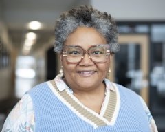 Joanne Johnson, in glasses and a blue sweater vest smiles at the camera.