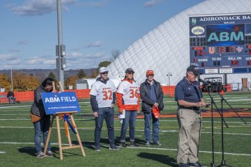 Members of ABM and Utica University stand on the football field near a sign that says ABM Field. 