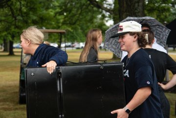 Students in blue shirts carry large pieces of luggage onto campus for Move-In Day 2025.