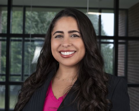 Ana Gabriela de Oliveira Rosa in a pink top and black blazer, stands in front of a window and smiles.