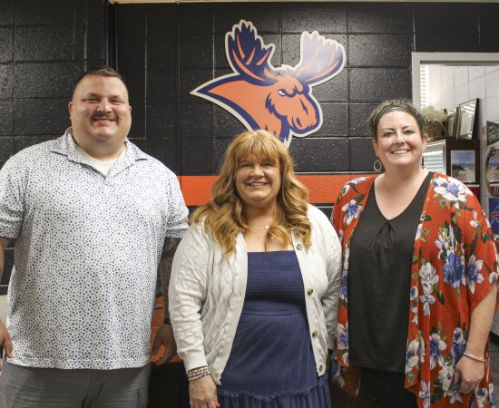 The Student Involvement and Leadership Team stand in front of a painted brick wall with an orange moose on it.