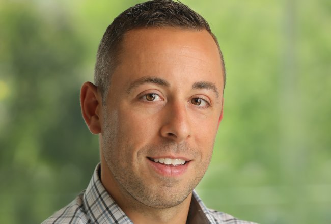 Matt Coppola stands with arms folded in front of a green background.