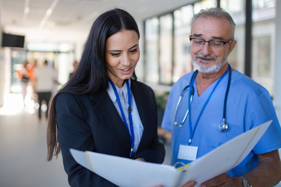Healthcare administrator review files with a provider in the hallway of a healthcare facility.