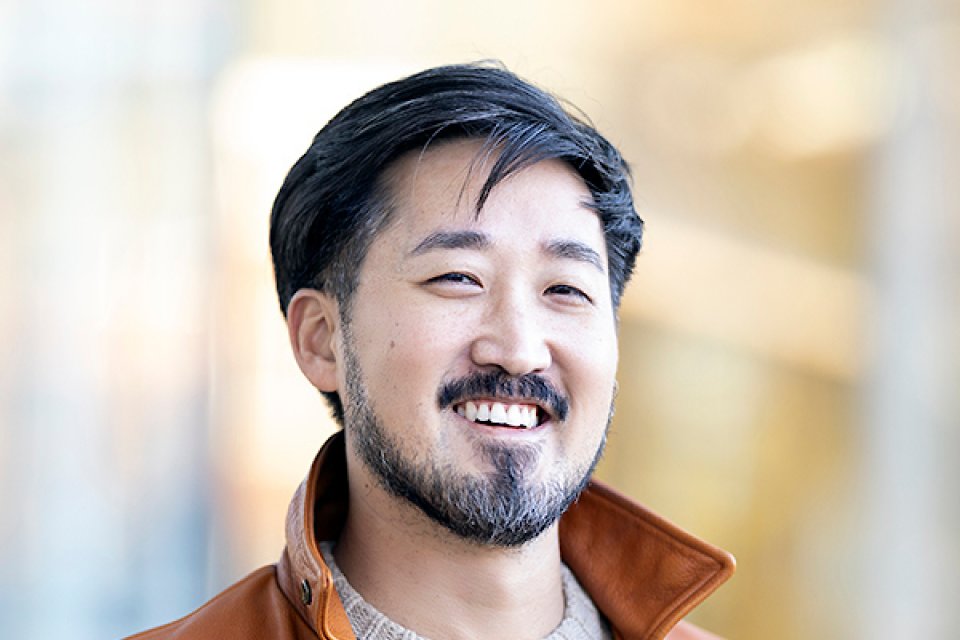 Jason Koo, in beige sweater and orange jacket, smiles at the camera.