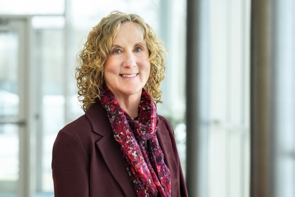Dr Ann Damiano, in a purple blazer and scarf, stands by glass windows.